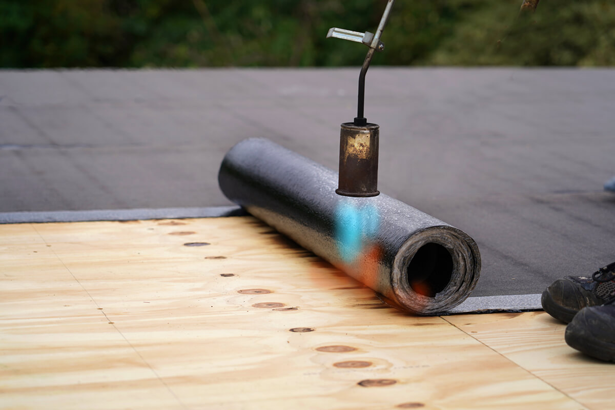 Waterproof membrane welded onto flat roof by torch.